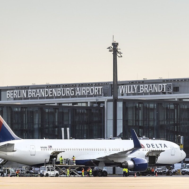 Eine Delta Airline Maschine steht vor einem Gates des Flughafens BER und wird entladen.