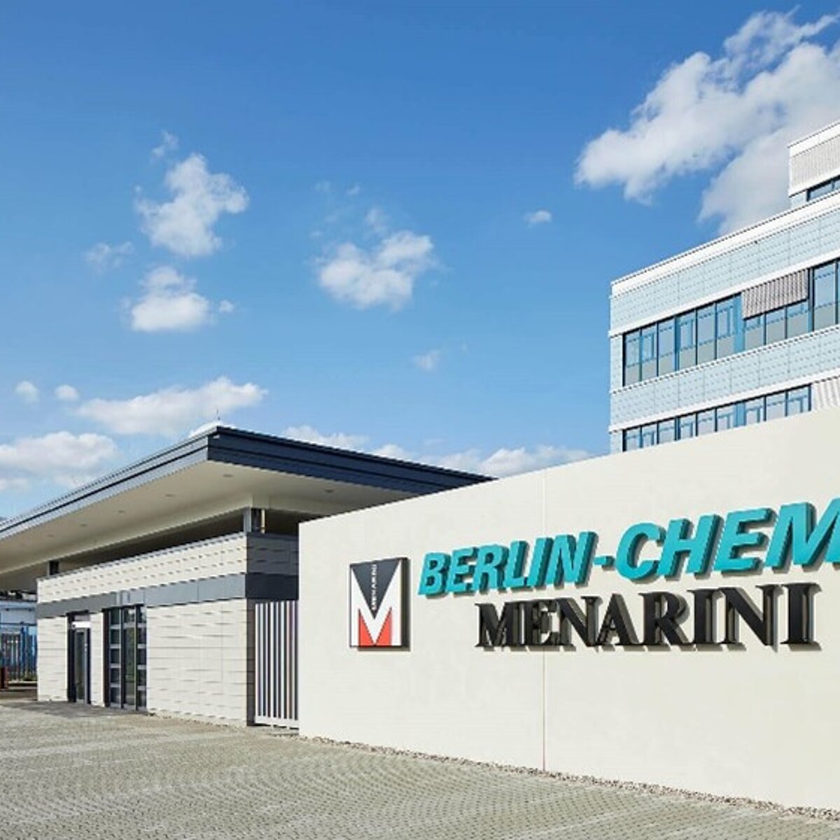 Man sieht das Eingangstor und einen Teil vom Hauptgebäude von Berlin-Chemie, einem Berliner Pharma-Unternehmen, Das Logo des Unternehmens ist am Eingang angebracht , in türkiser Schrift