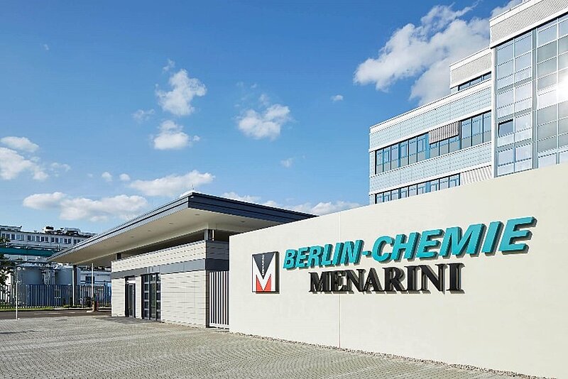 Man sieht das Eingangstor und einen Teil vom Hauptgebäude von Berlin-Chemie, einem Berliner Pharma-Unternehmen, Das Logo des Unternehmens ist am Eingang angebracht , in türkiser Schrift