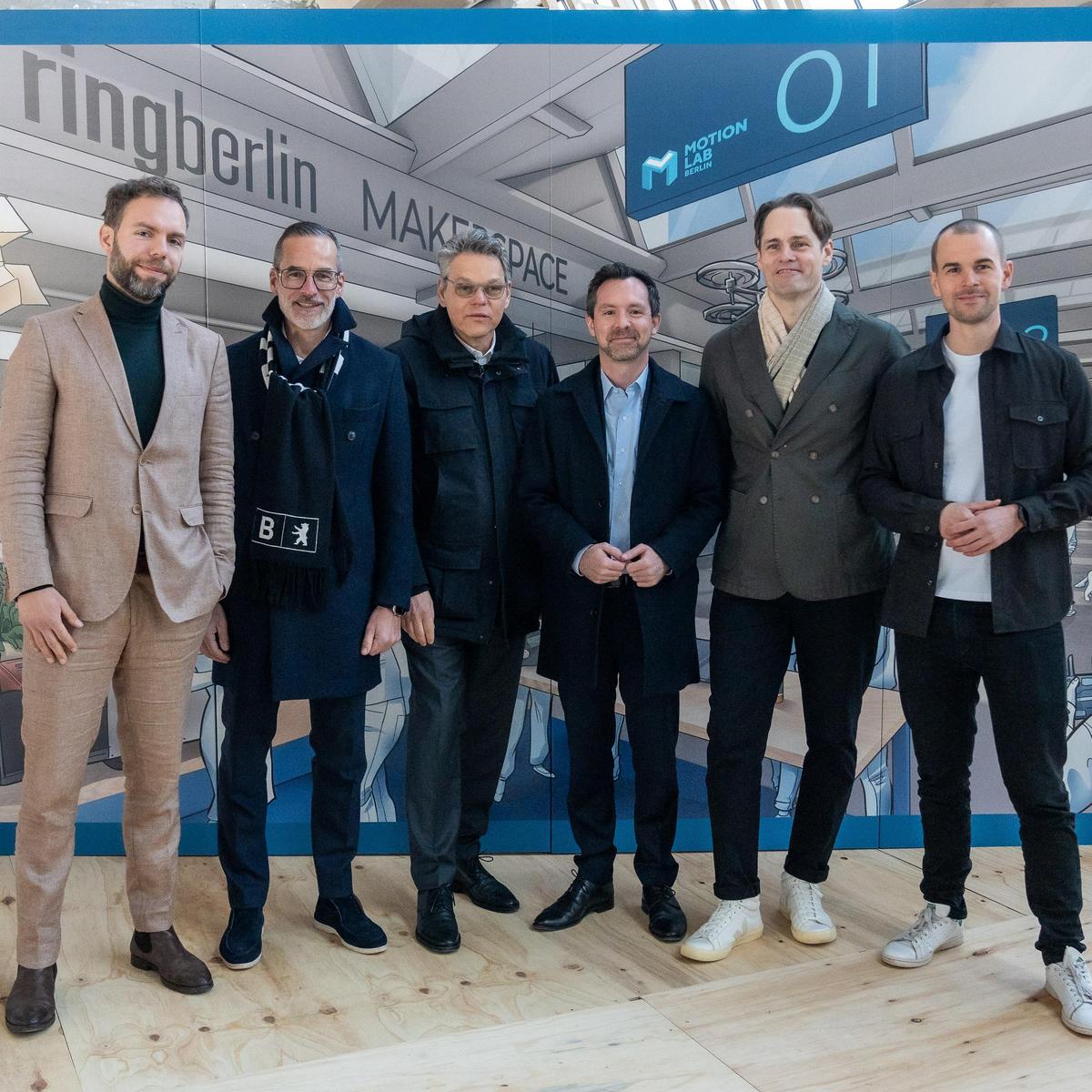 Zur Übernahme von MotionLab.Berlin stehen folgende Personen vor einer Werbewand zusammen: Dr. Moritz Heuberger, MdB Bündnis 90/Die Grünen, Dr. Stefan Franzke, Geschäftsführer Berlin Partner, Jörn Oltmann, Bezirksbürgermeister Tempelhof-Schöneberg, Berlin, Dr. Severin Fischer, Staatssekretär in der Senatsverwaltung für Wirtschaft, Energie und Betriebe, Berlin, Matthias Menger, Geschäftsführer ringberlin/KOIMO Development, Fridtjof Gustavs, Co-Founder und Managing Director MotionLab.Berlin
