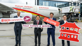 Bild zeigt 4 Männer vor einem Flugzeug der Hainan Airlines für die feierliche Bekanntmachung der Erweiterung der Flugverbindungen auf viermal pro Woche. Die Männer halten dazu Schilder vor sich, die das verdeutlichen.