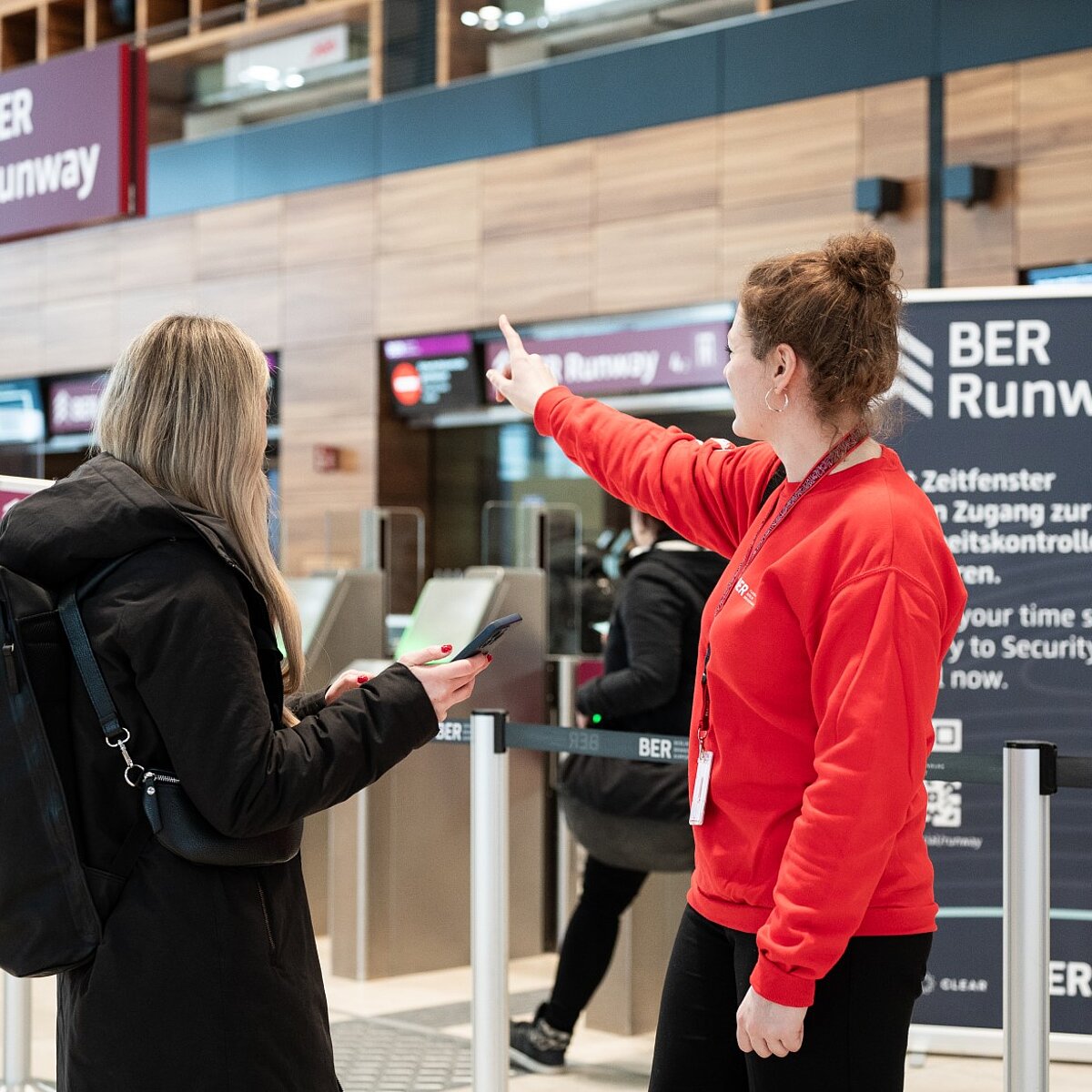 Fluggast mit einem BER Mitarbeiter vor dem BER Runway - Securitycheck zum News-Thema: BER gewinnt Airport Innovation Award 2023