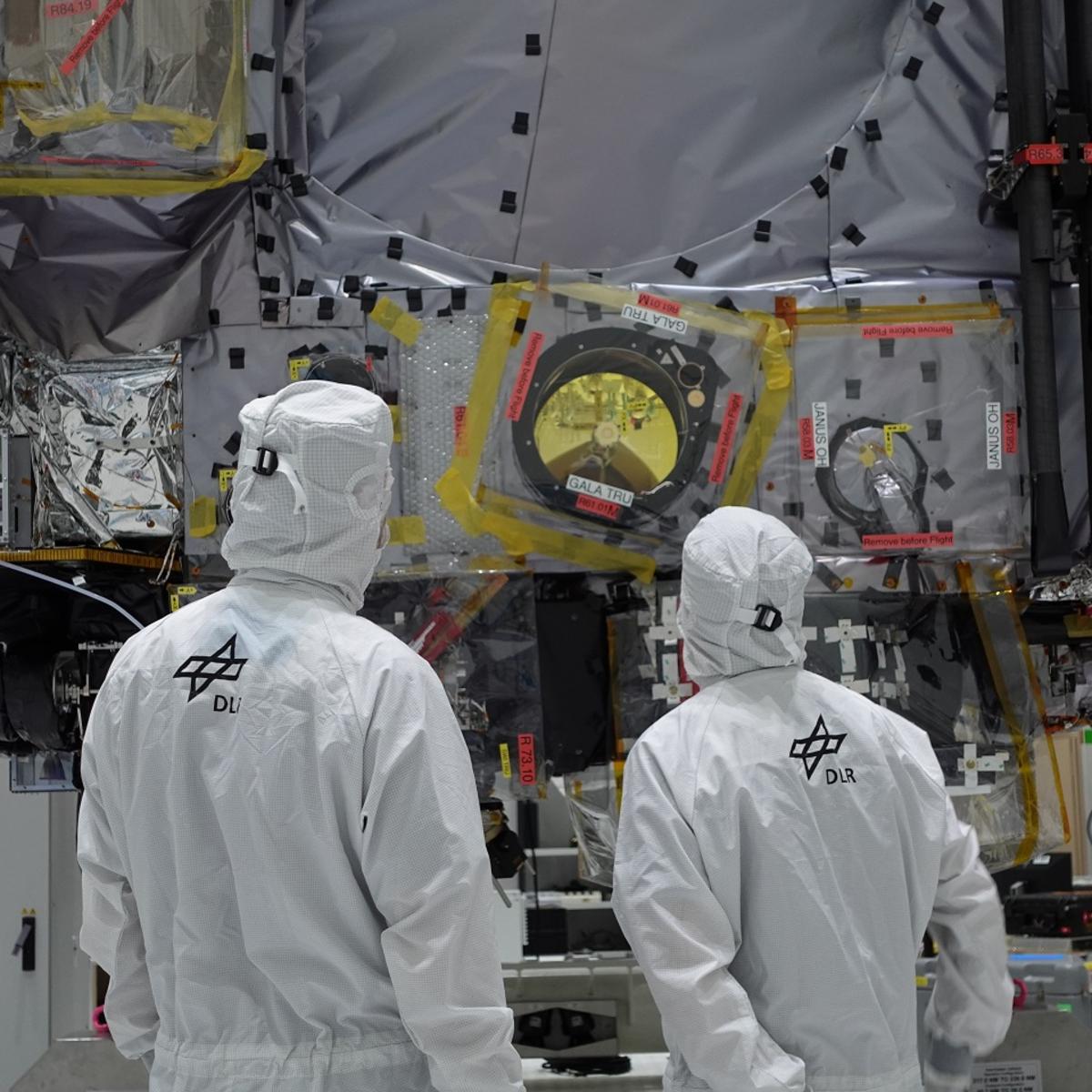 2 Personen im weißen Schutzanzug stehen vor der optischen Kamera und Laser-Altimeter für ESA-Mission JUICE