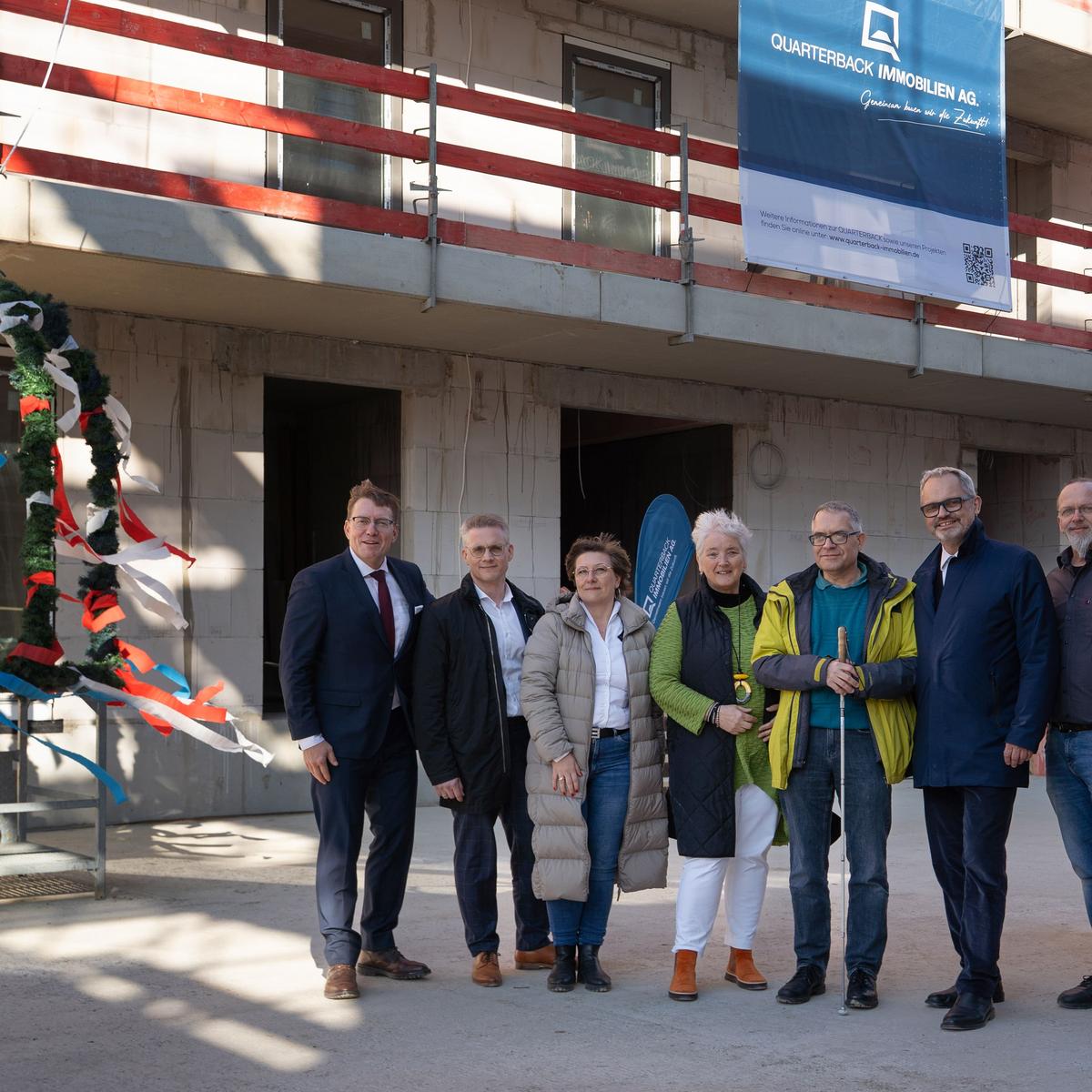 Vor dem Wohnquartier beim Richtfest sind folgende Personen nebeneinander zu sehen: v.l.n.r. Steffen Hanke Niederlassungsleiter Potsdam QUARTERBACK Immobilien AG, Michael Fuchs, Geschäftsführer Adolf Lupp GmbH, Stefanie Löwe-Koch, Head of Office Management Office   East/West & Residential HIH Gruppe, Michaela Wiezorek, Bürgermeisterin Königs Wusterhausen Georg Hanke, Ortsvorsteher Ortsteil Königs Wusterhausen Henrik Thomsen, Vorstand QUARTERBACK Immobilien AG Nils Witschonke, Oberbauleiter Adolf Lupp GmbH