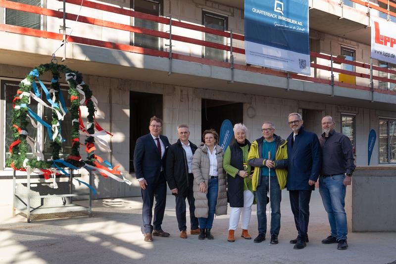 Vor dem Wohnquartier beim Richtfest sind folgende Personen nebeneinander zu sehen: v.l.n.r. Steffen Hanke Niederlassungsleiter Potsdam QUARTERBACK Immobilien AG, Michael Fuchs, Geschäftsführer Adolf Lupp GmbH, Stefanie Löwe-Koch, Head of Office Management Office   East/West & Residential HIH Gruppe, Michaela Wiezorek, Bürgermeisterin Königs Wusterhausen Georg Hanke, Ortsvorsteher Ortsteil Königs Wusterhausen Henrik Thomsen, Vorstand QUARTERBACK Immobilien AG Nils Witschonke, Oberbauleiter Adolf Lupp GmbH