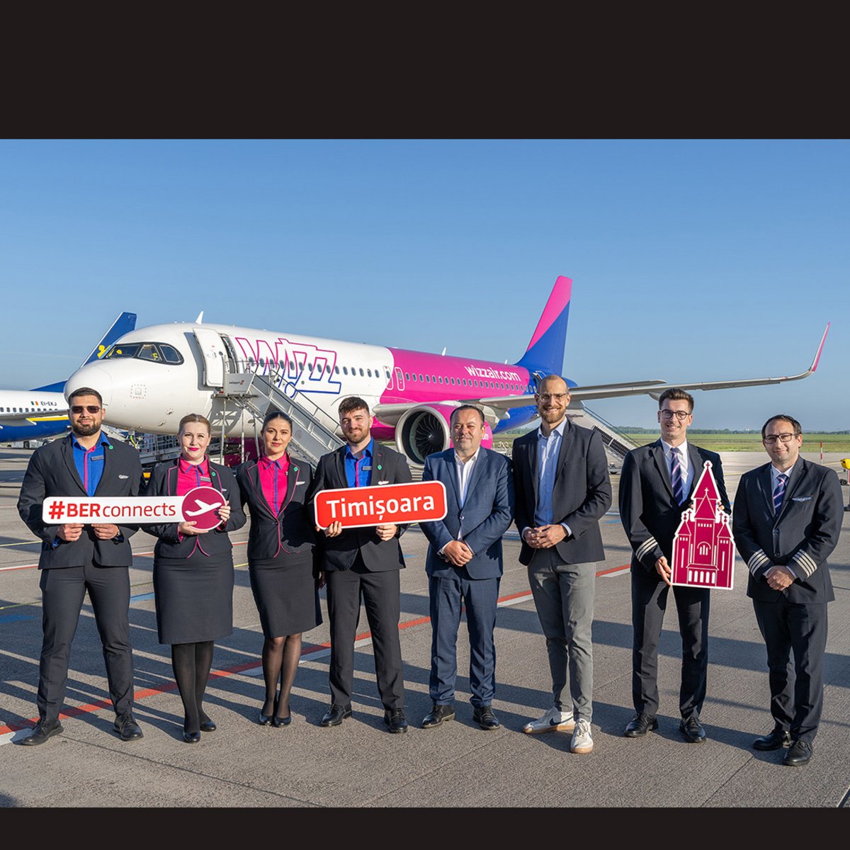 Folgende Personenen halten Werbeschilder vor einer Wizz Air Maschine:  Alin Popoviciu, Vice President Timiș County Council (5.v.l) und Johannes Mohrmann, Business Development Aviation der Flughafen Berlin Brandenburg GmbH (6.v.l.), die Crew von Wizz Air.