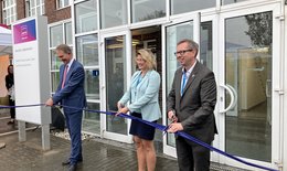 Das Bild zeigt eine Frau und zwei Männer Personen,  die feierlich ein Band zerschneiden zur Eröffnung eines neuen Firmenstandorts.