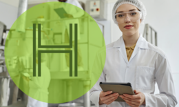 Bild zeigt eine Forscherin mit tablet in der Hand im Vordergrunf, die in die Kamera schaut. Im Hintergrund sieht man etwas verschwommen zwei weitere Forscher an einem größeren technischen Gerät hantieren. Über das Foto ist ein grüner Kreis mit einem großen "H" gelegt, als Symbol für Wasserstoff.